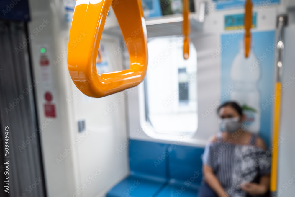 Closeup of yellow hand grip on a subway train with a woman passenger on the background Closeup of yellow hand grip on a subway train with a woman passenger on the background