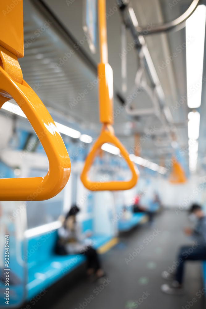 Closeup of yellow hand grip on a subway train with passenger on the background