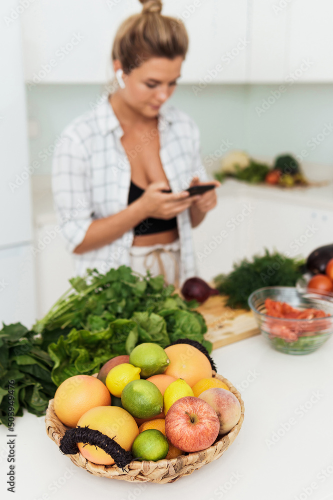 Basket full of different fruits and young woman with a smartphone on background