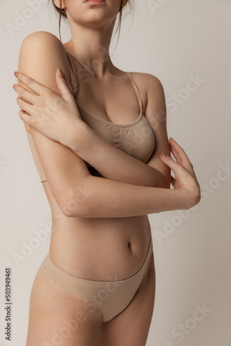 Tender beauty. Young slim woman posing in beige underwear isolated over grey studio background photo