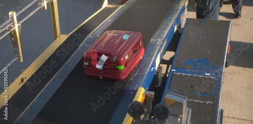 one red hard sided suitcase travelling on a luggage or baggage conveyer belt being loaded onto an airplane on the airport tarmac in Albuquerque New Mexico as seen from window seat of airplane 