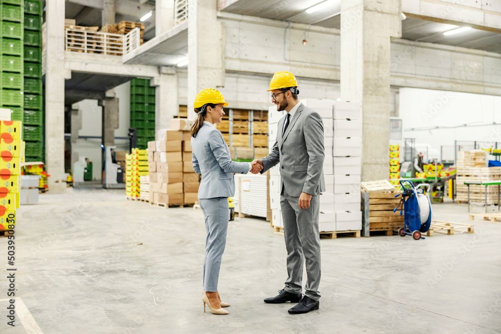 Businesspeople stand in the company's warehouse and shake hands. - obrazy, fototapety, plakaty 