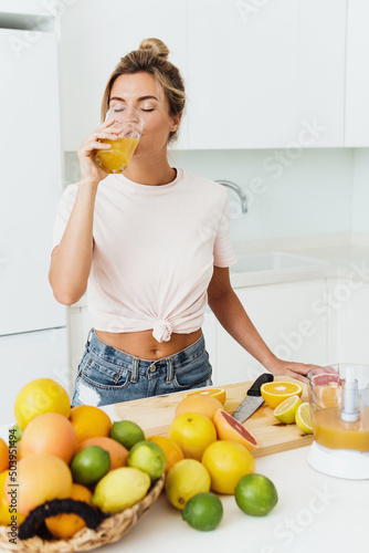 Bild auf Leinwand Woman drinking freshly squeezed homemade orange juice in white kitchen
