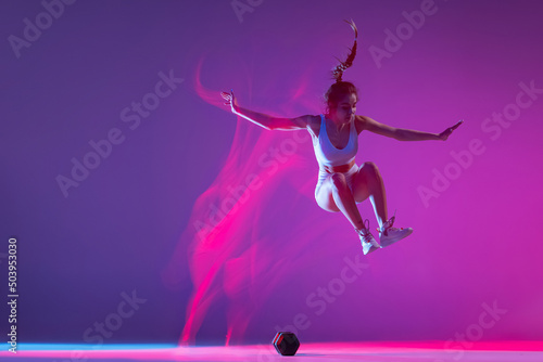 Young girl  athlete training isolated on blue studio background in mixed pink neon light. Healthy lifestyle  sport  motion and action concept.