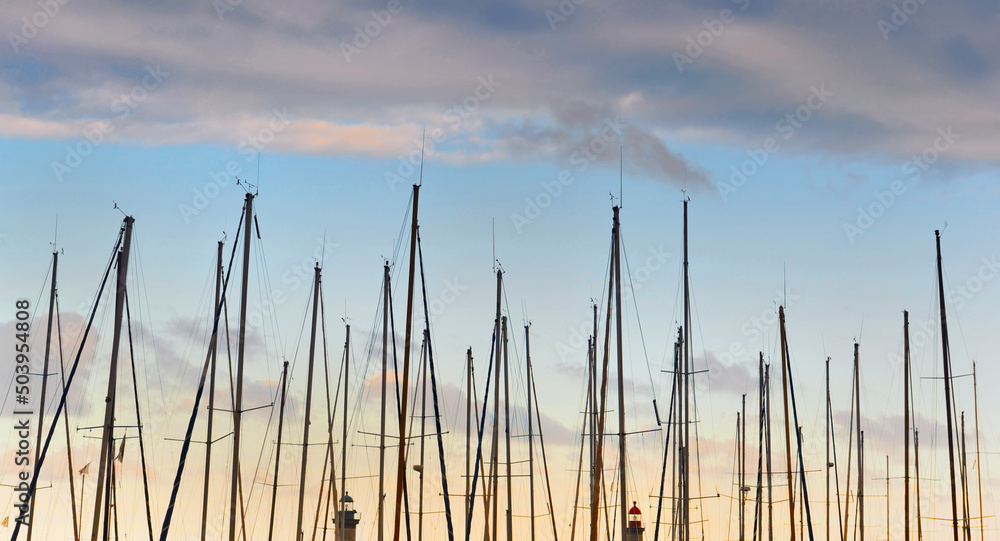 closeup view of row of sailboat masts in a harbor under a colorful cloudy sky