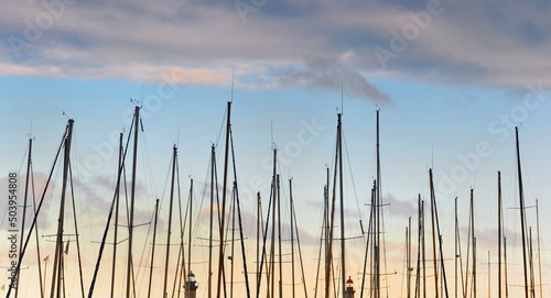 closeup view of row of sailboat masts in a harbor under a colorful cloudy sky