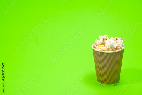 Popcorn in a glass on a green background with space for text.