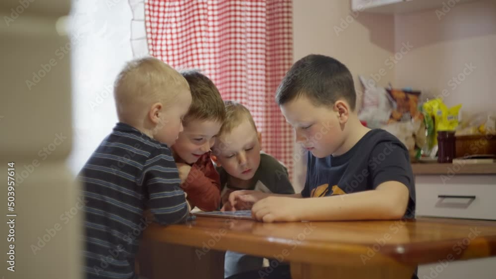 A group of Caucasian boys sitting on the Internet on a tablet. Children play in gadgets at the table in the kitchen at home. A group of Caucasian boys sitting on the Internet on a tablet. Children play in gadgets at the table in the kitchen at home.