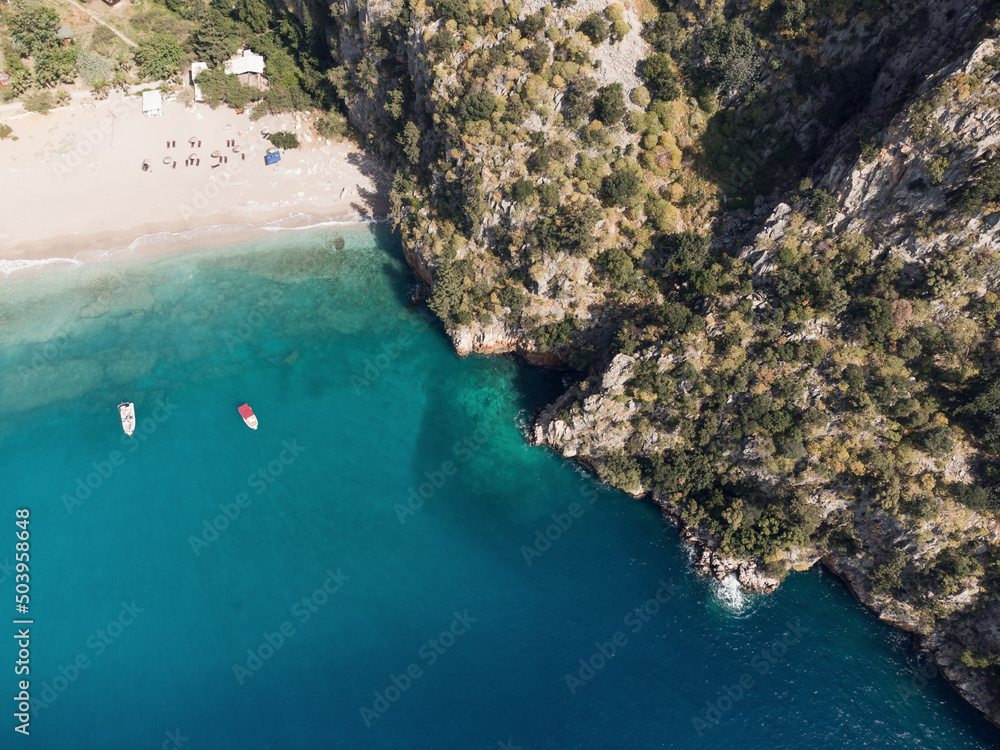 Aerial top view of sea waves and white boats on the beach with turquoise sea water. Sea waves on the wild rocky coast. Seascape. Travel concept. Aegean Sea, Turkey. Postcard view. Drone shot