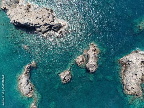 Aerial top view of sea waves hitting rocks on the beach with turquoise sea water. Sea waves on the wild rocky coast. Seascape. Travel concept. Aegean Sea, Turkey. Postcard view. Drone shot