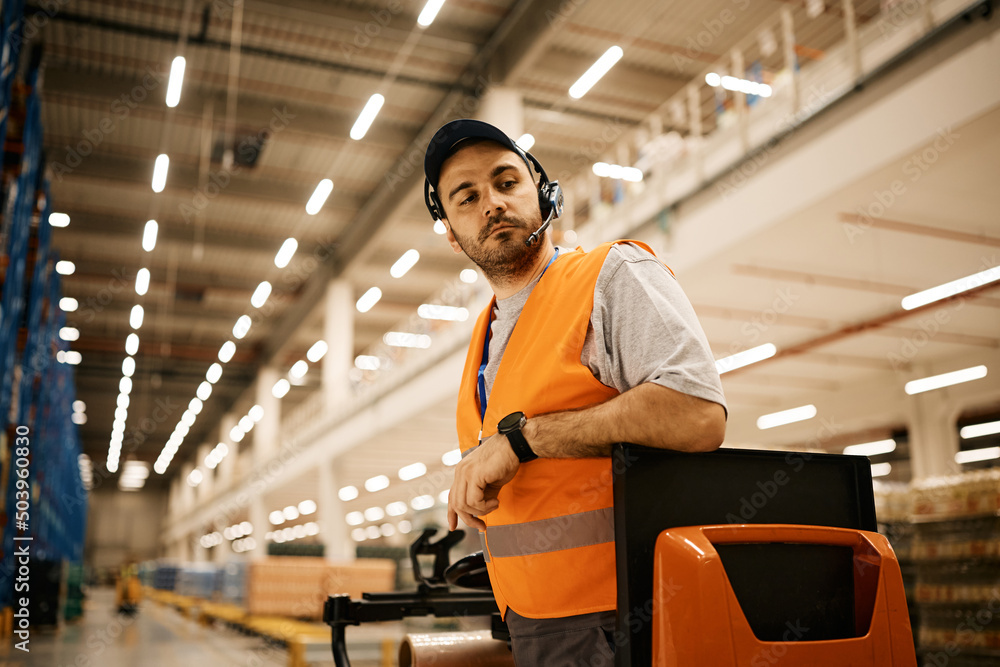 Fototapeta premium Warehouse worker driving pallet jack at storage compartment.