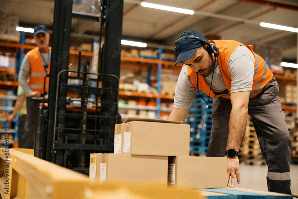 Warehouse worker organizing shipment boxes with his coworker at distribution compartment. Warehouse worker organizing shipment boxes with his coworker at distribution compartment.
