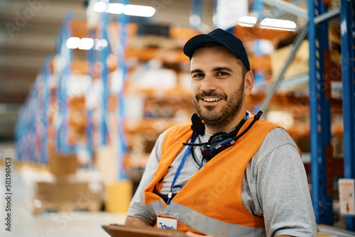 Happy warehouse worker working at storage compartment and looking at camera.