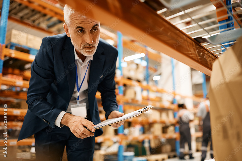 Mature warehouse manager checking stock of packages at storage compartment. Mature warehouse manager checking stock of packages at storage compartment.