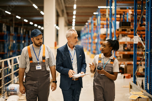 Young warehouse workers talk to their manager while walking through storage compartment. photo