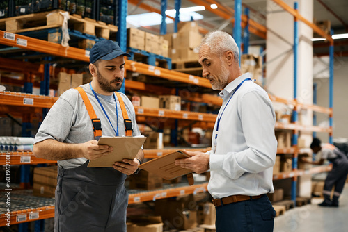 Warehouse worker and mature foreman using digital tablet at storage compartment.