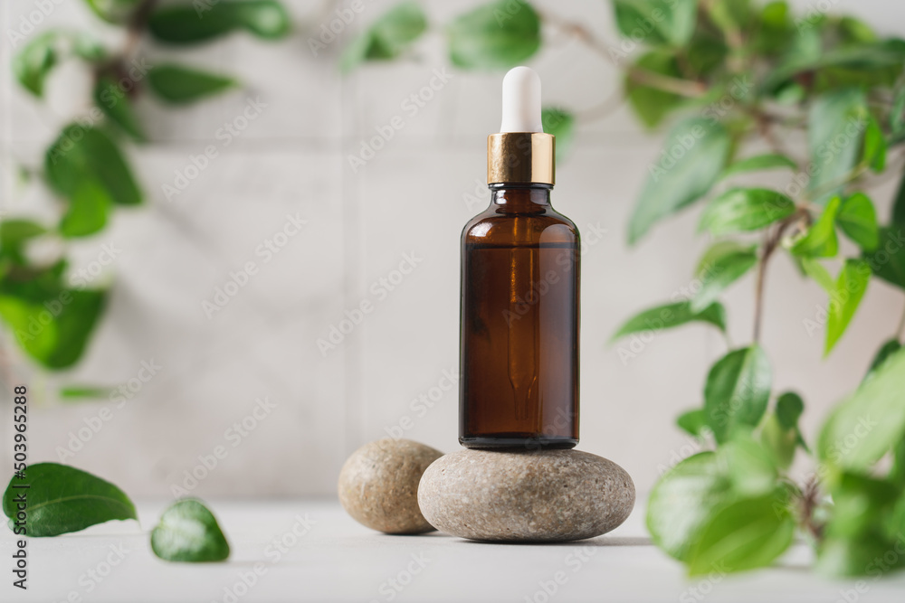 Amber glass dropper bottle on podium with green plants on light background. Skincare products , serum, natural cosmetic. Beauty concept for face and body care Amber glass dropper bottle on podium with green plants on light background. Skincare products , serum, natural cosmetic. Beauty concept for face and body care