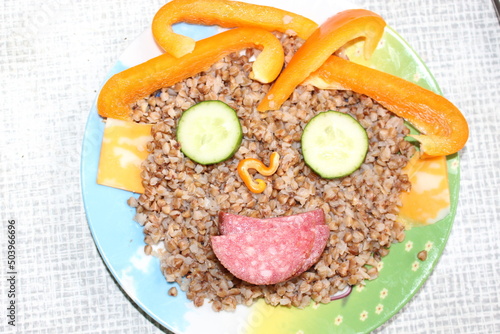 Wallpaper Mural Breakfast for a child is decorated in the form of a funny face in a plate. Buckwheat, pepper, cucumber, cheese, sausage are good for the body Torontodigital.ca