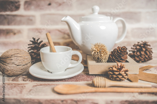 Tea concept, white teapot with white tea cup with dry leaves on wooden background.