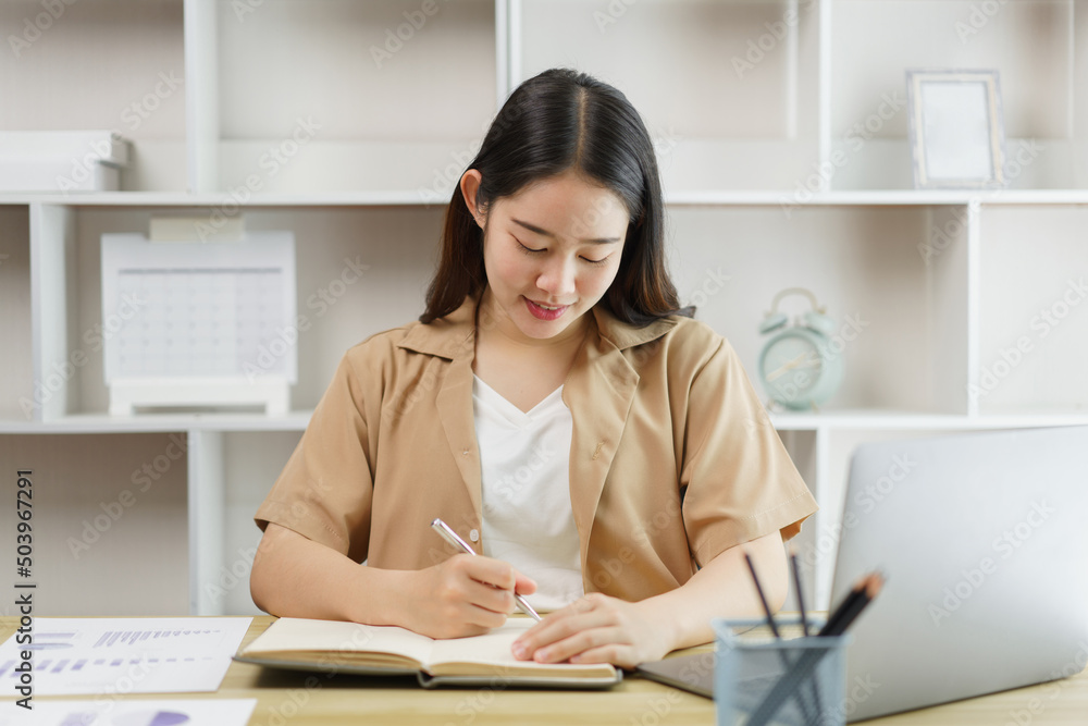Online lifestyle concept The female home worker writing down the information presenting on the notebook. Online lifestyle concept The female home worker writing down the information presenting on the notebook.
