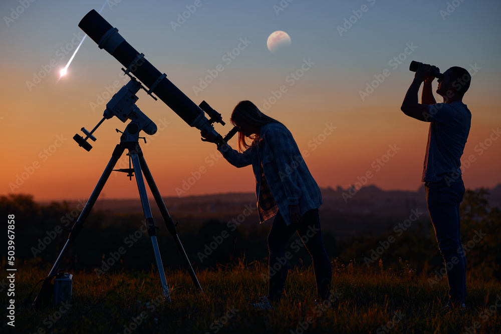 Couple stargazing together with a astronomical telescope, looking at planets, stars, lunar eclipse and meteor shower.