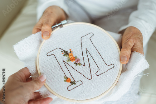 Woman giving an embroidery hoop with the letter M to her senior mother