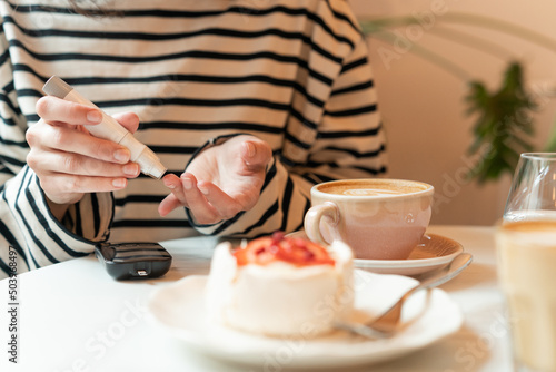 Diabetic woman sitting at a table testing blood sugar level in a cafe before eating
