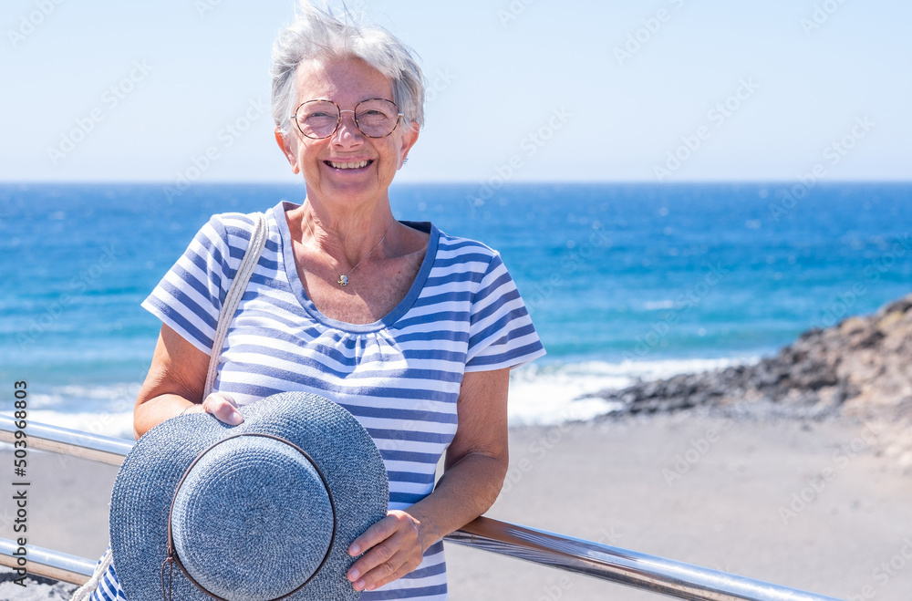 Fototapeta premium Happiness and good mood in senior smiling woman in outdoors sea excursion. Attractive white haired lady dressed in blue expressing freedom and joy. Horizon over water