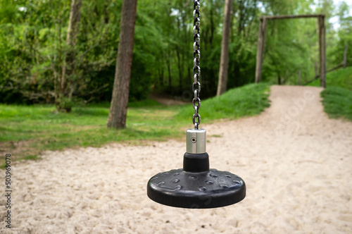 Children swing or zipline, with a round plastic seat attached to a metal chain, on the playground. © koldunova