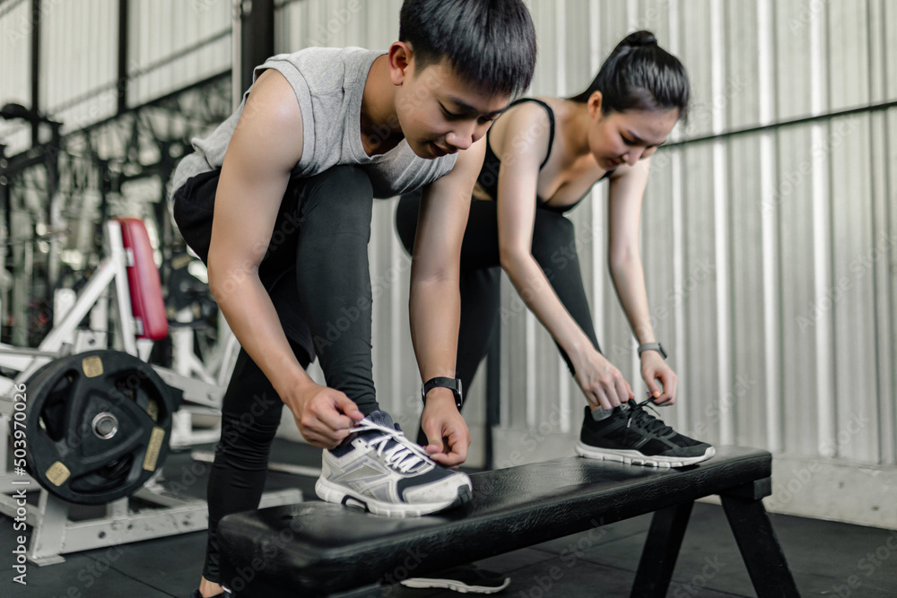 exercise concept The man and woman in the sport club resting one of their feet on the black bench and trying to tie up their shoelace