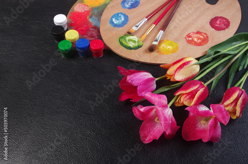  Attributes of the arts. Painting. Artist palette, brushes, paints and a bouquet of tulips. On a black background. 