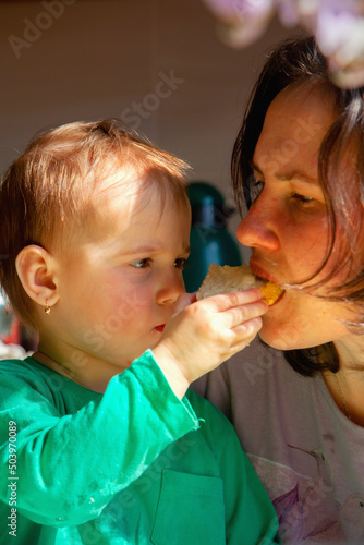 Funny portrait of cute little child girl shares food and feeds her mother