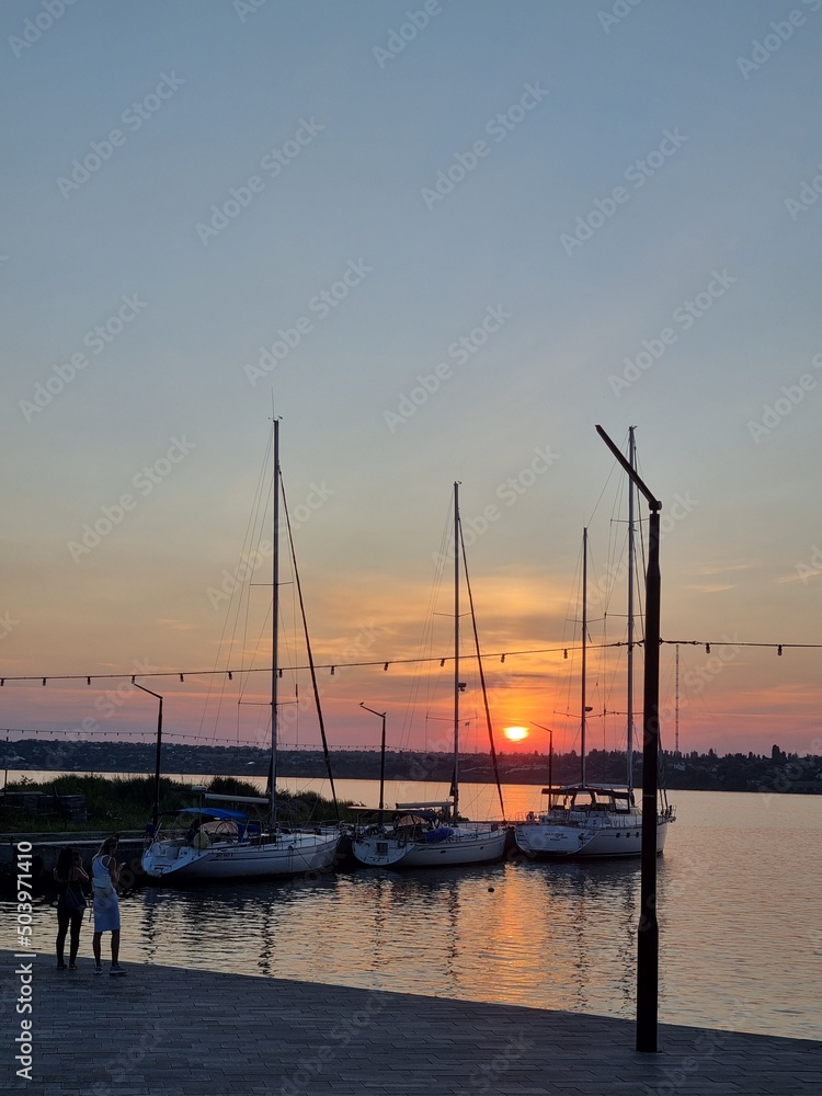 Mykolaiv, Ukraine - . September 4, 2021. Gorgeous Golden hour sunset with boats and yachts at dusk on the river shore. the sun rays of the evening light and sunlight. People walking at the Yachts-club