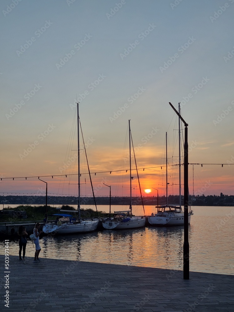 Mykolaiv, Ukraine - . September 4, 2021. Gorgeous Golden hour sunset with boats and yachts at dusk on the river shore. the sun rays of the evening light and sunlight. People walking at the Yachts-club