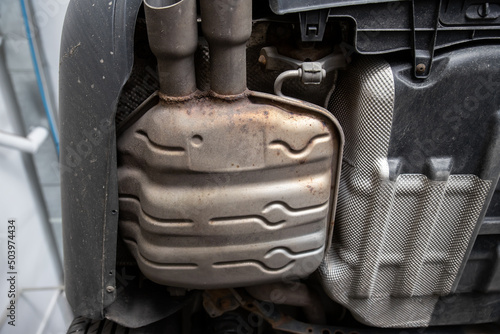 Close-up detail bottom view of car part metal exhaust muffler pipe with rusty stains. Lifted vehicle check-up maintenace service, repair and fix at automotive workshop photo