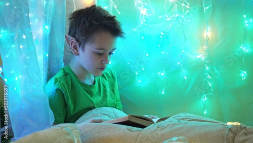 a teenager in an elf costume reads a book sitting on a bed decorated with garlands. reading a book on Christmas night
