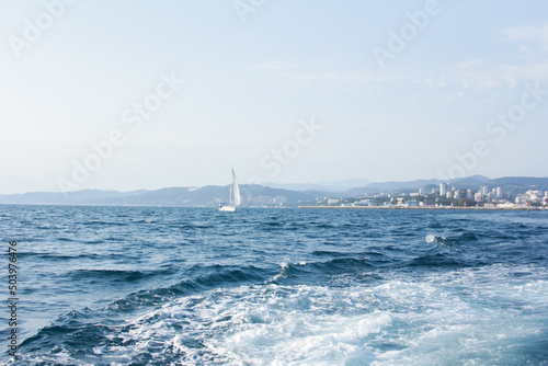 seascape with waves and a sailboat and mountains in the background 