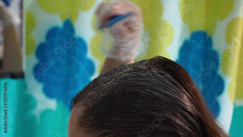 a woman dyes her hair with a brush. smearing the paint on . close-up of hair and a brush in the reflection in the mirror