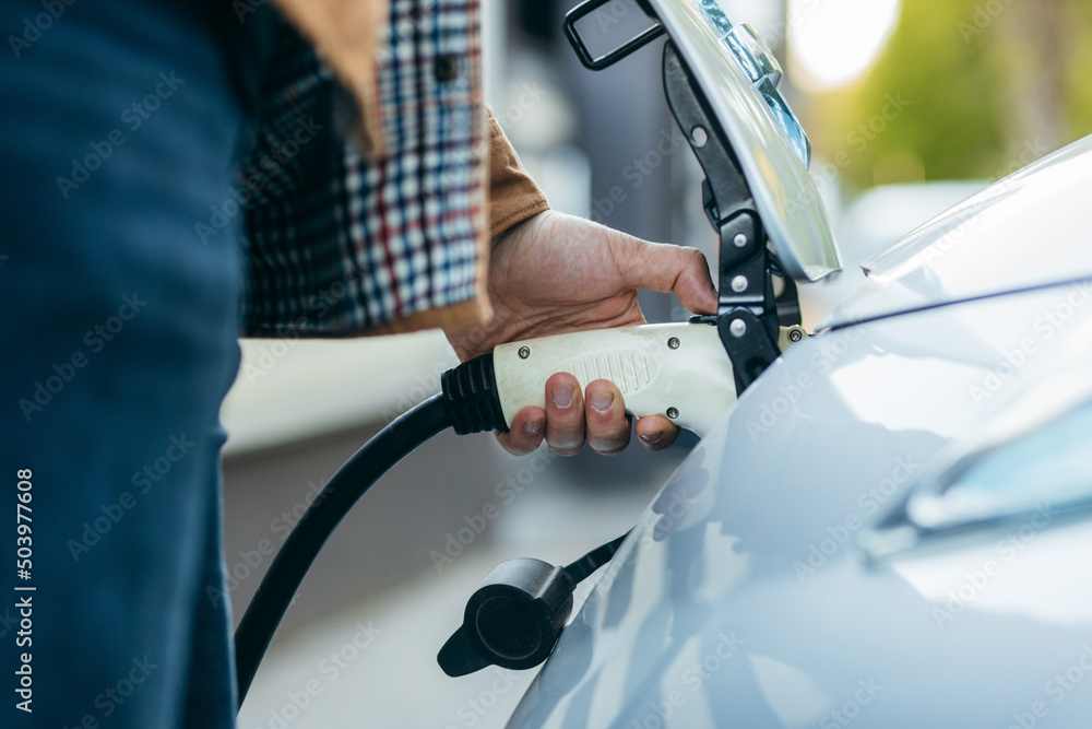 Man holding power supply cable at electric vehicle charging station. Close-up
Man holding power supply cable at electric vehicle charging station. Close-up