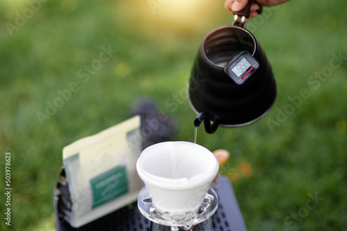 Young man pouring coffee in cup, morning breakfast on open air. traveler camping for first time, new experience to rest with tent. Nature, leisure, no rush, peace and calmness concept