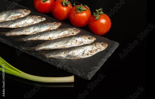 Salty tracing paper with vegetables on a serving board. Small fish with onions and tomatoes. Delicious breakfast ideas