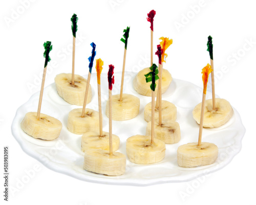 Fotografi Banana slices appetizer on a white plate with color-topped cellophane toothpicks