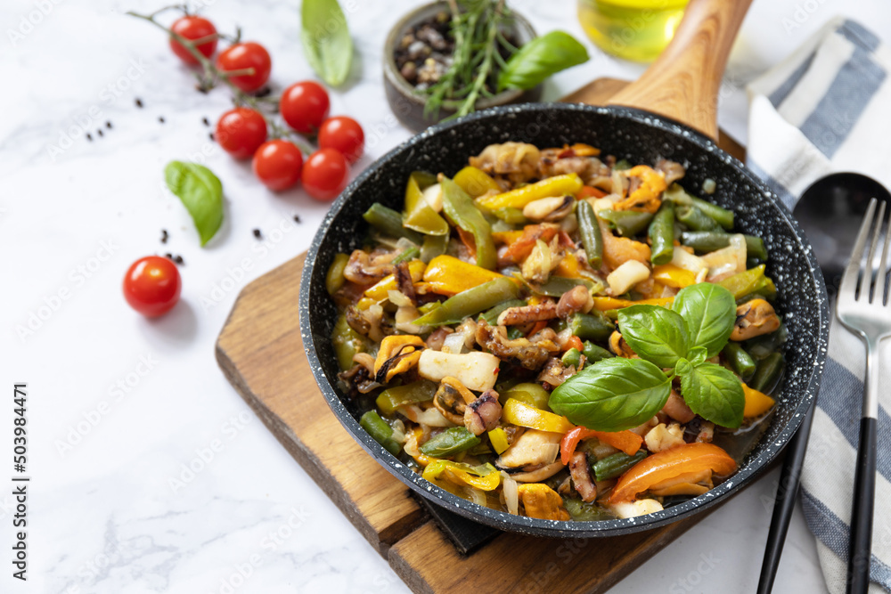 Vegetarian wok stir fry. Seafood shrimps, calamari, cuttlefish stewed with vegetables and garlic sauce on a marble tabletop. Copy space. Vegetarian wok stir fry. Seafood shrimps, calamari, cuttlefish stewed with vegetables and garlic sauce on a marble tabletop. Copy space.