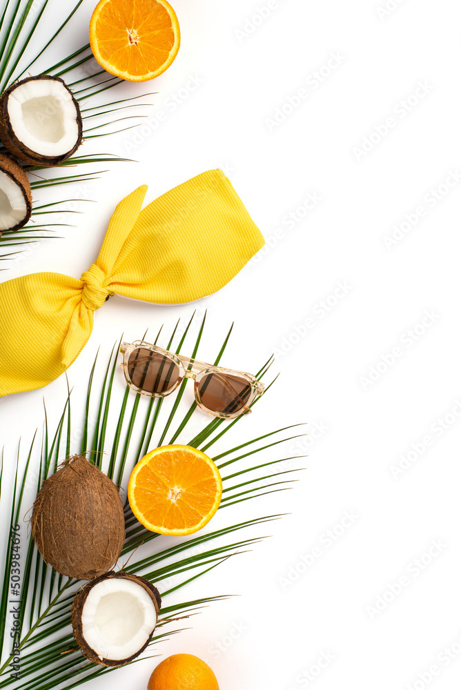 Summer holidays concept. Top view vertical photo of yellow swimwear sunglasses coconuts oranges and palm leaves on isolated white background with copyspace Summer holidays concept. Top view vertical photo of yellow swimwear sunglasses coconuts oranges and palm leaves on isolated white background with copyspace