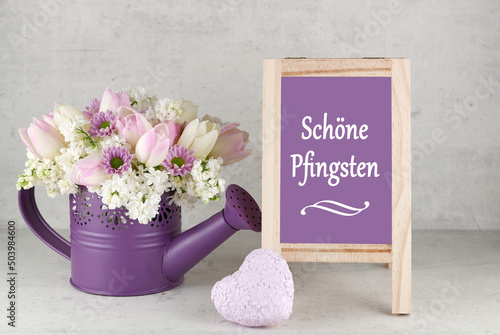 Blumenarrangement mit Flieder und Tulpen und dem Text Schöne Pfingsten auf einer Kreidetafel.