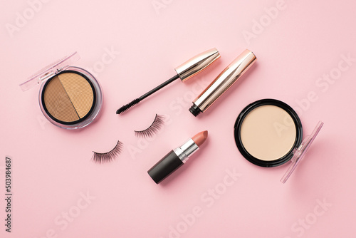 Make up concept. Top view photo of compact powder contouring palette lipstick false eyelashes and mascara on pastel pink background