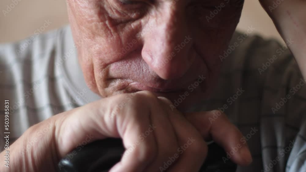 Close-up portrait of caucasian sad pensioner 70 years old sitting meditating with walking stick. Slow motion. The theme is the elderly. Selective focus Close-up portrait of caucasian sad pensioner 70 years old sitting meditating with walking stick. Slow motion. The theme is the elderly. Selective focus