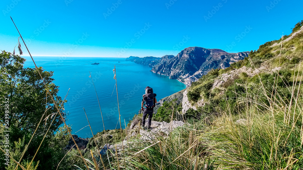 Fototapeta premium Man with panoramic view from hiking trail Path of Gods between coastal towns Positano and Praiano. Trekking in Lattari Mountains, Apennines, Amalfi Coast, Campania, Italy, Europe. Mediterranean Sea