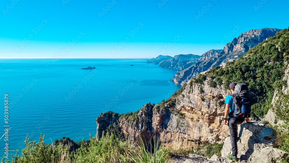 Man with panoramic view from hiking trail Path of Gods between coastal towns Positano and Praiano. Trekking in Lattari Mountains, Apennines, Amalfi Coast, Campania, Italy, Europe. Mediterranean Sea