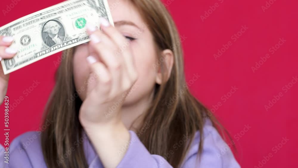 portrait of a caucasian young woman 20 years old looking at a 100 dollar bill. American paper money with a face value of 100 dollars. American currency. Devaluation and inflation concept. portrait of a caucasian young woman 20 years old looking at a 100 dollar bill. American paper money with a face value of 100 dollars. American currency. Devaluation and inflation concept.